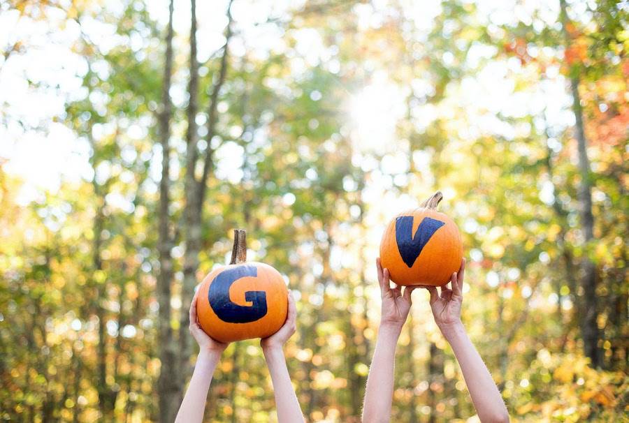 People holding up two pumpkins, one has a blue G and another has a blue V